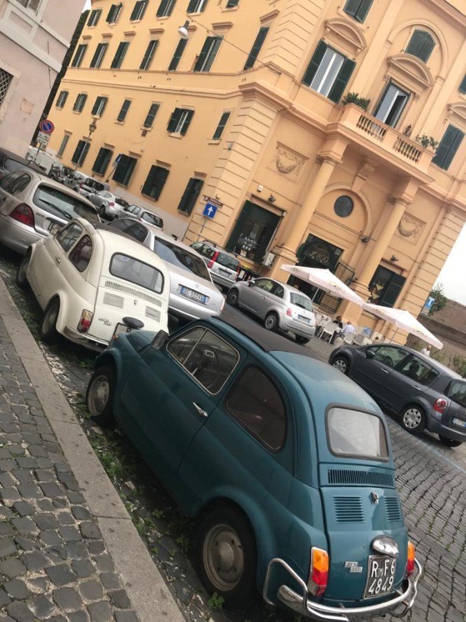 Teal and white vintage Fiat 500 cars parked on a cobblestone street among peach-colored buildings